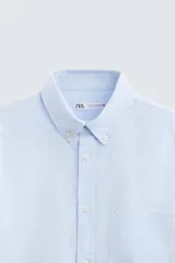 Camisa celeste a rayas verticales, de corte relaxed fit, confeccionada en lino y algodón. Tiene cuello abotonado, manga larga con puños abotonados, bolsillo de parche en el pecho y cierre frontal con botones.