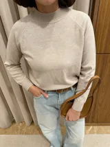 Buzo de punto en color beige, con cuello redondo alto y mangas largas con diseño raglán. Presenta puños y cuello acanalados.