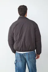 Campera acolchada de color gris oscuro, con diseño de cuello tipo camisa, cierre frontal con cremallera y bolsillos laterales. Presenta puños y ruedo con elástico.