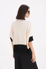 Sweater de punto bicolor con cuello alto, mangas cortas y corte holgado. Presenta un diseño con bloque de color negro en el ruedo y las mangas, y un detalle decorativo de cinto de cuero sintético con hebilla en el frente.
