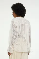 Blusa oversize blanca de encaje calado semitransparente, con cuello mao, cierre frontal de botones, mangas largas abullonadas con puños fruncidos y aberturas laterales en el ruedo.