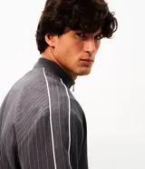Campera deportiva de helanca color gris oscuro, con diseño de raya diplomática fina, cuello bomber, cierre frontal y bordados en el pecho.
