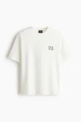 Remera de algodón blanca de corte holgado, con cuello redondo y estampa pequeña con el texto "PALM NOIR" en el pecho.