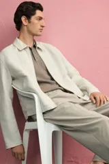 Pantalón de corte relajado color beige claro, con cintura elástica ajustable con cordón oculto y pliegues frontales. Presenta bolsillos laterales y bolsillos traseros ribeteados.