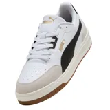 Championes Puma modelo Shuffle Downtown OG, de diseño urbano con base blanca, detalles en negro y suela de goma color caramelo. Presentan refuerzos en gamuza gris en la puntera y el talón, con el logo de la marca en dorado.