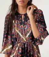 Vestido corto de manga larga con estampado estilo paisley en tonos azul marino, rojo y crema. Presenta un escote redondo con cordones ajustables, cintura elástica y mangas abullonadas.