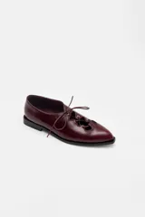 Zapato acordonado de cuero color bordó, con punta fina y diseño estilo oxford. Presenta cordones al tono y detalles de ojales metálicos dorados.