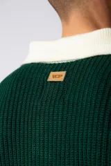 Sweater de punto con textura waffle en color blanco, con cuello polo en contraste color verde oscuro y cierre frontal de botones. Presenta un bordado decorativo en el pecho y un corte relajado.