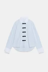 Camisa de algodón con cuello solapa y puños en color blanco a contraste. Presenta cierre frontal con alamares negros y bajo asimétrico redondeado.