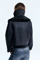 Campera de denim negro con forro de piel ecológica en el cuerpo y mangas con matelassé. Presenta doble cuello, uno de ellos desmontable, cierre frontal con botones metálicos y bolsillos tipo plaqué.