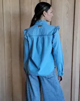 Camisa de denim azul con volados en el frente, cuello y hombros, de manga larga y corte clásico. Confeccionada en algodón.