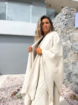 Ruana tejida en color crudo con diseño de trenzas y textura en relieve. Presenta un corte amplio y envolvente, ideal para usar como capa sobre otras prendas.