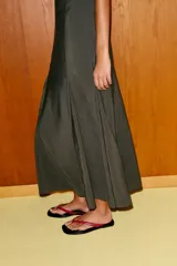 Vestido midi color verde oscuro, confeccionado en tejido fluido. Presenta cuello redondo, manga sisa y bajo con línea evasé y pliegues. Tiene cierre lateral con cremallera oculta y cierre en la espalda con abertura y botón.