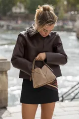 Bolso mini shopper de diseño trenzado en color beige, con asas de mano y correa bandolera extraíble en tono marrón. Presenta detalle de pespuntes en contraste y cierre interior con cremallera.