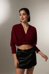 Blusa cropped de color negro, con cuello en V, mangas largas con puños ajustados y detalle de frunces en el frente.