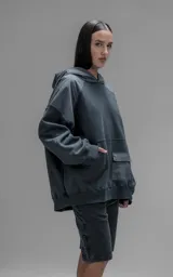 Hoodie oversize de algodón con diseño bicolor en gris oscuro y gris medio. Presenta capucha forrada, mangas raglán con recortes técnicos y un bolsillo frontal tipo canguro con un compartimento adicional con solapa.