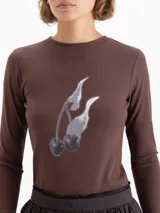 Remera de manga larga color marrón, confeccionada en tejido de punto suave y elástico. Presenta escote redondo a la base y una estampa frontal con diseño de cerezas.