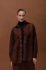 Camisa de cuero ovino color marrón, con diseño oversize, cuello camisero, cierre frontal con broches y detalle de flecos en el pecho. Presenta mangas largas con puños.