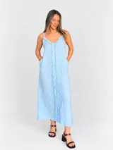 Vestido maxi celeste de lino, con escote en V, tiras finas regulables y detalles de flecos en la parte delantera. Presenta un calce fluido y fresco.