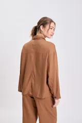 Chaqueta tipo camisa de lino color marrón, de corte holgado y manga larga. Presenta cuello camisero y cuatro bolsillos frontales con solapa.