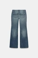 Jeans de tiro bajo con corte bootcut, confeccionados en denim con efecto lavado. Presentan costuras verticales marcadas en el frente, cierre frontal con cremallera, gancho metálico y detalle de trabilla con botones en la cintura.
