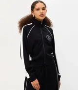 Campera deportiva de cuello alto y cierre frontal, color negro con franjas blancas en las mangas y costuras decorativas contrastantes. Cuenta con bolsillos laterales y puños ajustados.