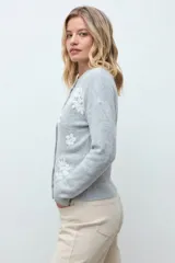 Cardigan de punto color gris melange con cuello redondo, cierre frontal de botones y delicado bordado floral en color blanco en la parte frontal.