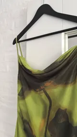 Vestido corto de tirantes finos con escote drapeado, confeccionado en tela semitransparente con estampado abstracto en tonos verdes y negros. Incluye un accesorio tipo pañuelo integrado al cuello.