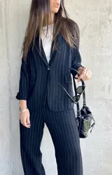 Blazer negro con finas rayas verticales blancas, solapas de muesca, cierre frontal con un botón y bolsillos laterales.