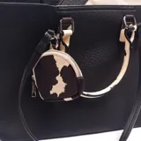 Cartera tipo tote de cuero sintético negro con textura granulada, asas de mano y detalles en estampado animal print tipo vaca, e incluye un monedero colgante a juego.