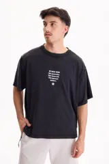 Remera oversize de manga corta en color negro con efecto acid wash. Presenta un pequeño estampado frontal con texto en inglés y un isotipo de flor en la parte superior del pecho.