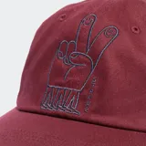 Gorro de béisbol color verde oliva con bordado frontal que incluye una flor sonriente con piernas y las letras "STANCE" rodeándola.