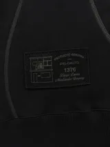Buzo blanco de manga larga con diseño holgado, cuello redondo y costuras externas visibles en contraste. Cuenta con una etiqueta decorativa en el frente inferior.