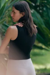 Top deportivo negro, corte cropped y ajustado, sin mangas y con cuello redondo. Presenta un detalle de nudo o torcido en el bajo frontal.