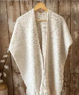 Ruana abierta de lana merino color marfil, con diseño tejido de textura granulada y flecos decorativos en el borde inferior.