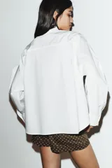 Camisa de popelín de algodón con cuello subido y detalle de aplicación tipo pañuelo anudado al cuello. Presenta manga larga con puños clásicos y cierre frontal mediante botones.