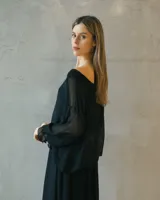 Vestido midi negro de seda italiana, con diseño de capas superpuestas, mangas largas translúcidas y silueta fluida.