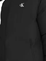 Campera puffer negra con capucha desmontable, cierre frontal con cremallera, bolsillos laterales con cremallera, puños y bajo elásticos, y logo de Calvin Klein bordado en el pecho.