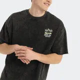 Remera de corte oversized en color negro con efecto lavado, cuello redondo y mangas cortas. Presenta un pequeño estampado gráfico en el pecho con el logo de la marca y palmeras.