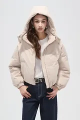 Campera puffer de color beige con cuello alto, capucha desmontable, cierre frontal y bolsillos laterales. Diseño de corte holgado con puños elásticos.