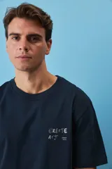 Remera blanca de algodón, de corte holgado y mangas cortas, con pequeño estampado azul en el pecho.