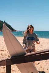 Remerón cropped color hueso con estampado frontal de tres cuadrados azules que contienen un hibisco, una ola y una concha marina, y la frase "Glassy Waves".