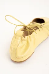 Chatitas de cuero color amarillo, con diseño acordonado en el empeine, puntera cuadrada y talón fruncido con cordón ajustable.