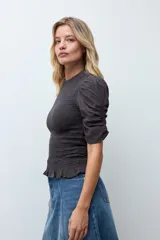 Blusa de color gris oscuro con diseño de punto smock en el cuerpo, cuello redondo y mangas cortas abullonadas con detalle de volados en el ruedo.