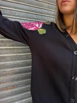 Cárdigan negro de algodón con escote en V y botones frontales. Presenta un aplique bordado de una rosa fucsia con hojas verdes en el hombro izquierdo.