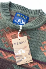 Buzo tejido de punto con diseño geométrico de estilo étnico en tonos verde, marrón y salmón. Presenta cuello redondo, puños y ruedo acanalados, con etiqueta de la marca Denali en el interior y en el frente.
