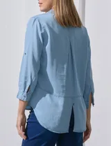 Camisa de tencel color celeste claro, con cuello con solapa, escote en V y abertura central con botones. Manga larga con presilla para ajustar el largo. El largo de espalda es mayor al delantero y tiene un tajo central.