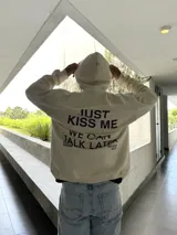 Canguro beige de algodón con capucha, cordones ajustables y estampa en pecho y espalda con la frase "Just Kiss Me We Can Talk Later".