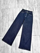 Pantalon jean de tiro alto con corte wide leg, confeccionado en denim azul oscuro con costuras en contraste. Presenta cierre frontal con botón metálico y bolsillos laterales.