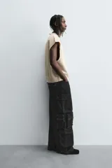 Pantalón cargo de denim lavado negro, corte relajado y tiro medio. Presenta múltiples bolsillos cargo con solapa y detalle de cierre en las perneras, además de bolsillos de vivo traseros. El bajo es ajustable con trabilla.